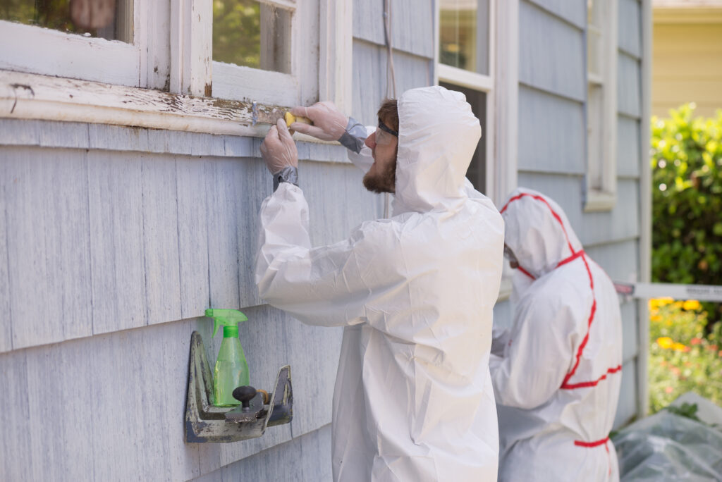 Two house painters in hazmat suits removing lead paint from an old house.