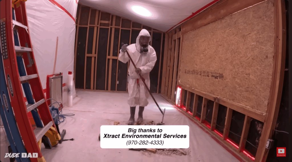 screenshot of a youtube video showing a worker in protective gear cleaning up asbestos-containing debris from insdie a home.